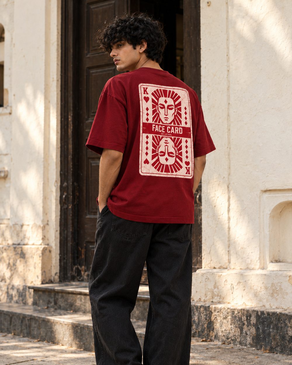 Face Card tee in maroon, full back print, standing in an old stone doorway