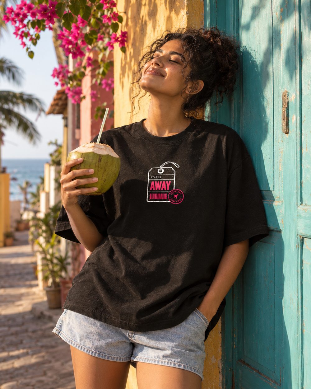 Out of Office tee, AWAY tag chest print, leaning on a wall with a coconut