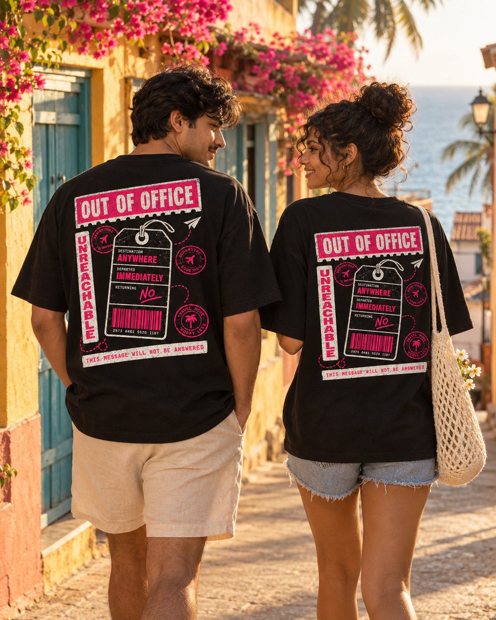 Two people in Out of Office tees walking a seaside lane, back prints